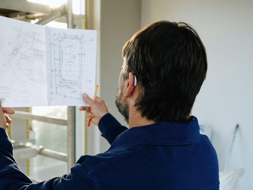 Man wearing a behind-the-ear hearing aid at work, the kind of listening situation assistive devices support, in Mesa, AZ